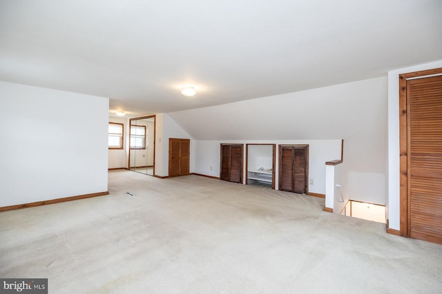 additional living space with baseboards, lofted ceiling, and light colored carpet