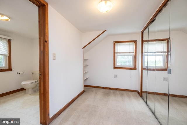 interior space featuring vaulted ceiling, ensuite bathroom, a closet, and baseboards