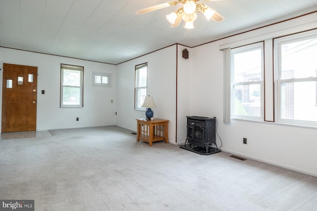 living area featuring carpet flooring, a ceiling fan, visible vents, baseboards, and a wood stove
