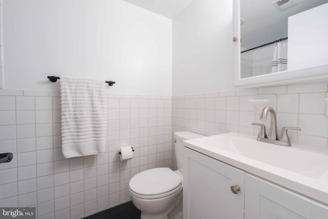 full bathroom featuring vanity, toilet, a wainscoted wall, tile walls, and visible vents
