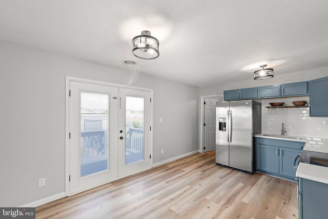kitchen featuring light wood-style floors, stainless steel refrigerator with ice dispenser, a sink, backsplash, and blue cabinetry