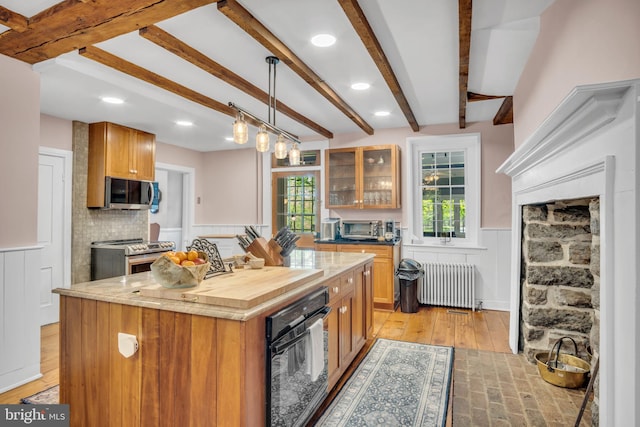 kitchen featuring brown cabinets, wainscoting, beam ceiling, radiator heating unit, and stainless steel appliances