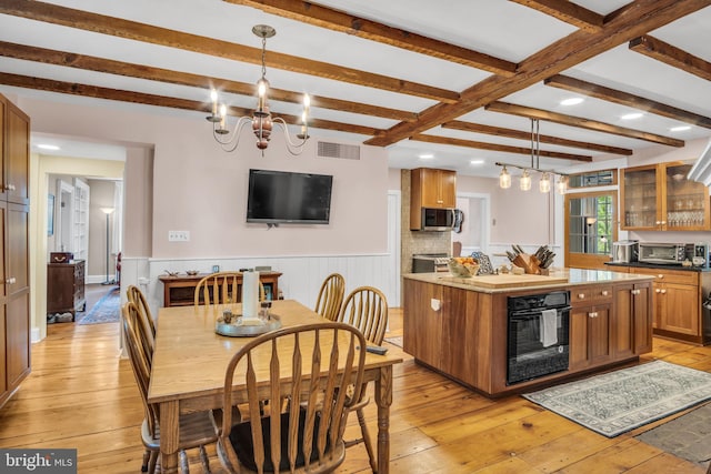 kitchen featuring brown cabinetry, stainless steel microwave, a notable chandelier, light wood-style floors, and oven