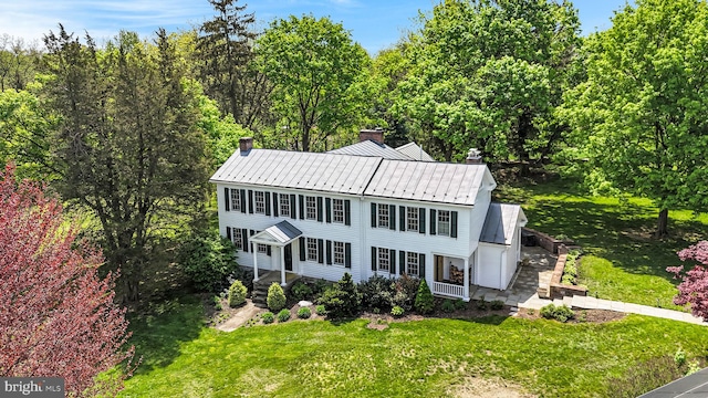 view of front of property featuring a standing seam roof, a chimney, a front lawn, and metal roof