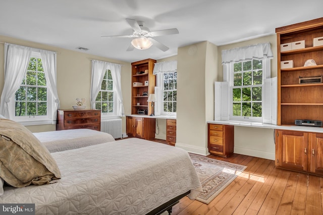 bedroom featuring visible vents, radiator, baseboards, light wood-style floors, and built in desk