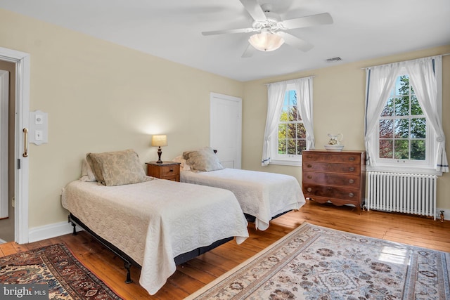 bedroom featuring a ceiling fan, visible vents, hardwood / wood-style flooring, baseboards, and radiator