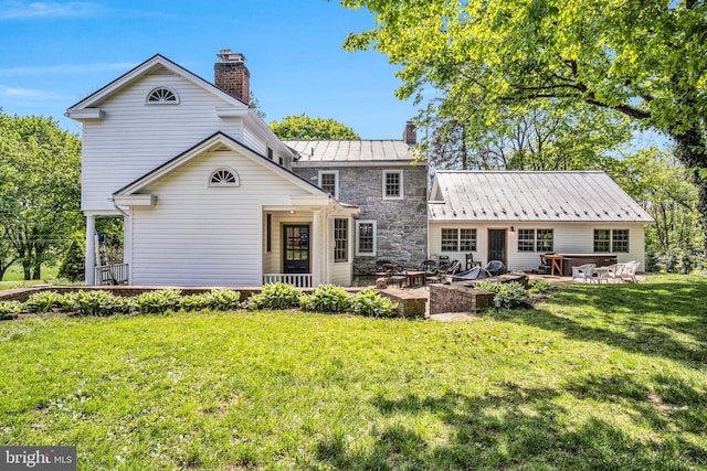 back of property with a standing seam roof, a chimney, a yard, a patio, and stone siding