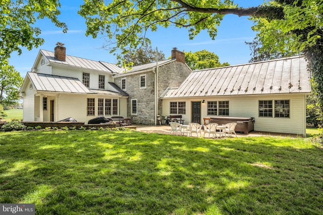 rear view of house with a hot tub, a patio area, a chimney, and a standing seam roof