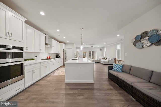 kitchen featuring wall chimney range hood, a ceiling fan, open floor plan, stainless steel appliances, and recessed lighting