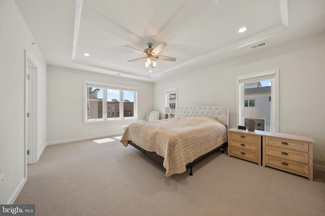 bedroom featuring light colored carpet, a raised ceiling, baseboards, and visible vents
