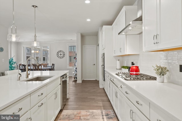 kitchen with decorative backsplash, wall chimney exhaust hood, white cabinets, a sink, and appliances with stainless steel finishes