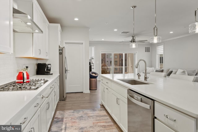 kitchen featuring wall chimney range hood, light countertops, white cabinets, a sink, and appliances with stainless steel finishes