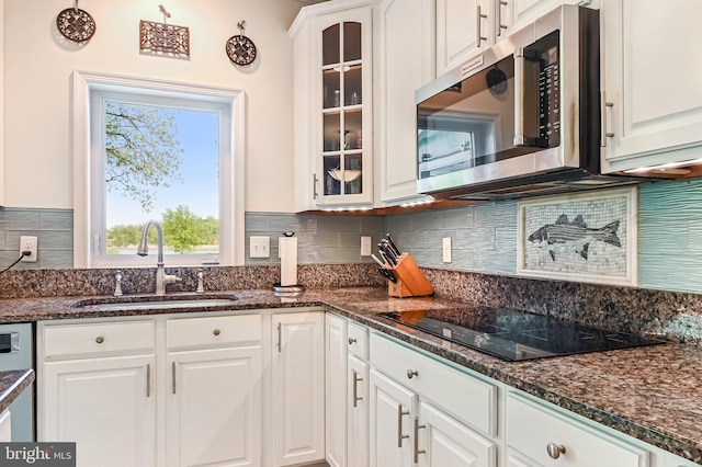 kitchen featuring white cabinets, black electric stovetop, a sink, stainless steel microwave, and glass insert cabinets