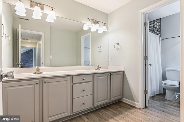 bathroom with visible vents, double vanity, wood finished floors, baseboards, and a sink