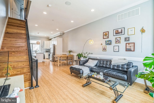living room with crown molding, light wood-style flooring, stairs, recessed lighting, and visible vents