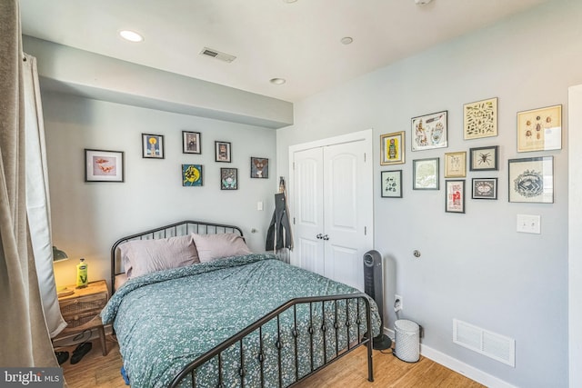 bedroom with visible vents, wood finished floors, and a closet