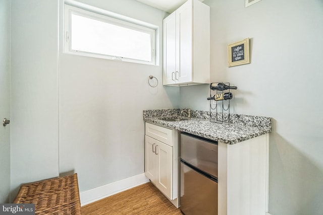 bar with light wood-style floors, baseboards, freestanding refrigerator, and a sink