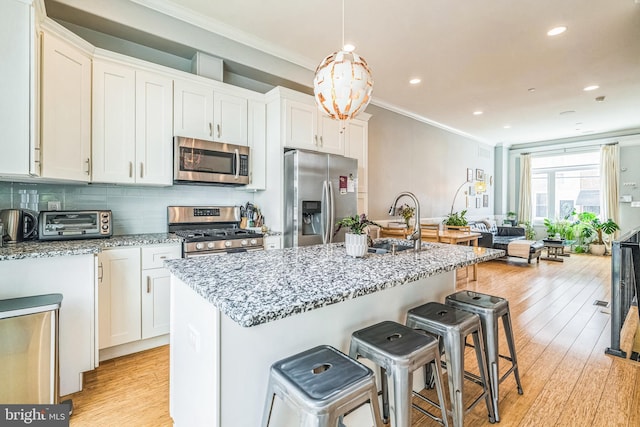 kitchen featuring a kitchen breakfast bar, crown molding, light stone countertops, white cabinets, and stainless steel appliances