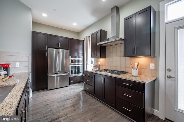 kitchen with light stone counters, decorative backsplash, wall chimney exhaust hood, and stainless steel appliances