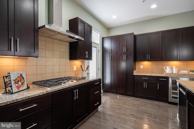 kitchen with wall chimney range hood, tasteful backsplash, stainless steel gas cooktop, light stone counters, and light wood finished floors