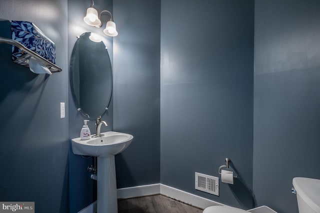 bathroom featuring baseboards, toilet, wood finished floors, and visible vents