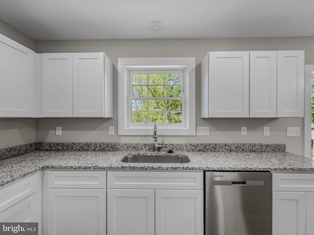 kitchen featuring stainless steel dishwasher, white cabinets, light stone counters, and a sink