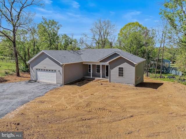 ranch-style home with a shingled roof, covered porch, an attached garage, and aphalt driveway