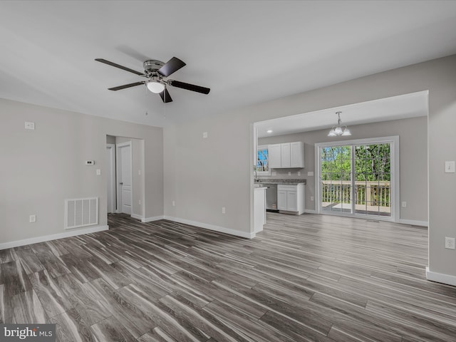 unfurnished living room with baseboards, ceiling fan with notable chandelier, wood finished floors, and visible vents