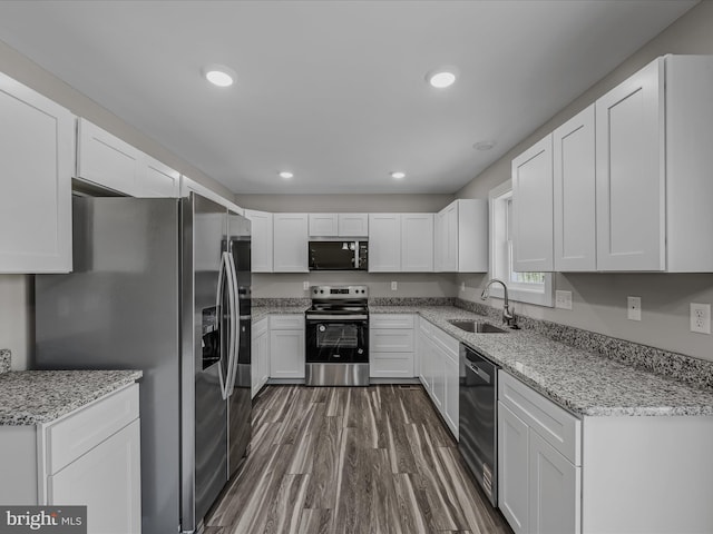 kitchen with wood finished floors, recessed lighting, white cabinets, a sink, and appliances with stainless steel finishes