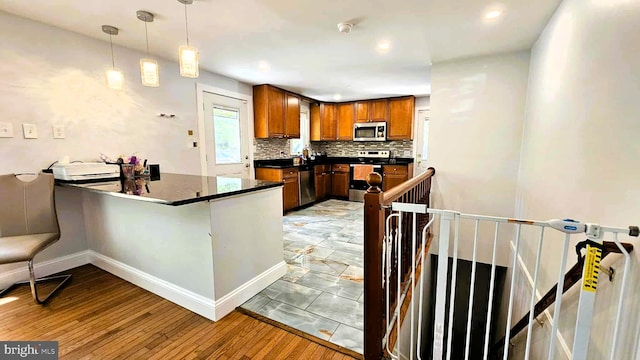 kitchen featuring backsplash, dark countertops, brown cabinets, a peninsula, and stainless steel appliances