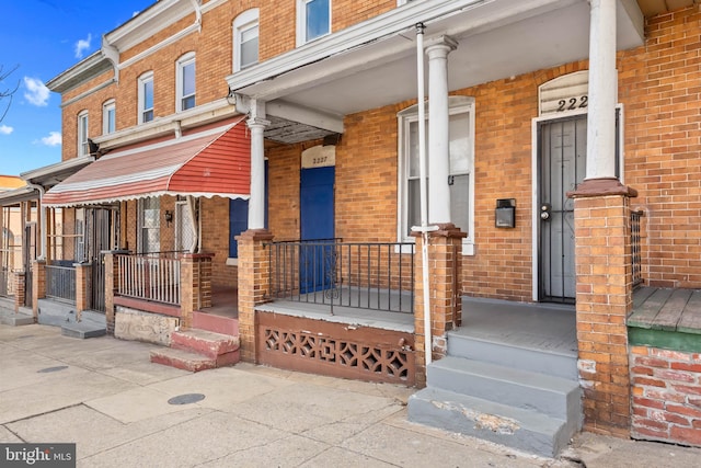 property entrance featuring a porch and brick siding