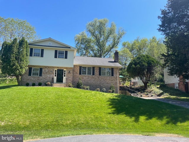 tri-level home featuring a front yard, a chimney, and brick siding