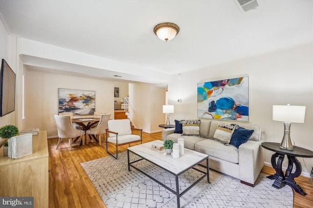 living room with stairs, light wood-style floors, and baseboards