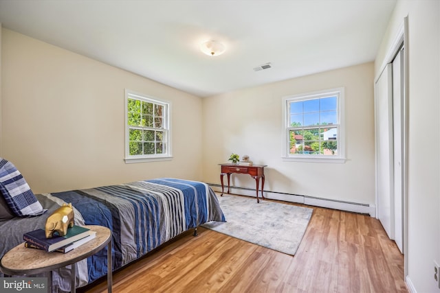 bedroom with a baseboard heating unit, wood finished floors, and a closet