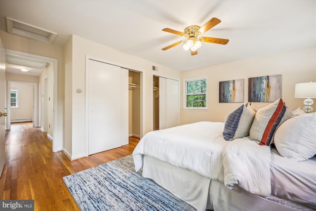 bedroom with attic access, multiple closets, a baseboard radiator, wood finished floors, and a ceiling fan