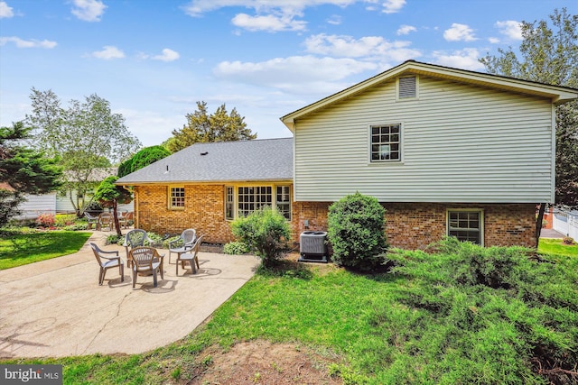 back of house with brick siding, a patio, central AC, and a lawn
