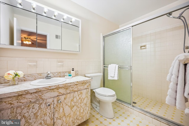 full bath featuring tile walls, a stall shower, toilet, vanity, and wainscoting