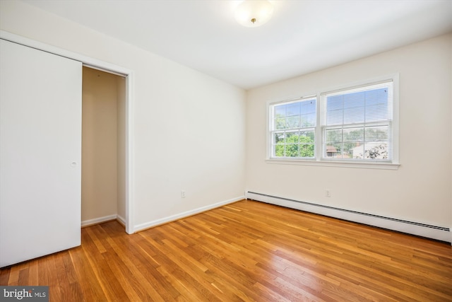 unfurnished bedroom with a baseboard radiator, light wood-style floors, and baseboards