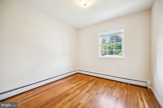 spare room featuring light wood-style floors, a baseboard heating unit, and baseboards