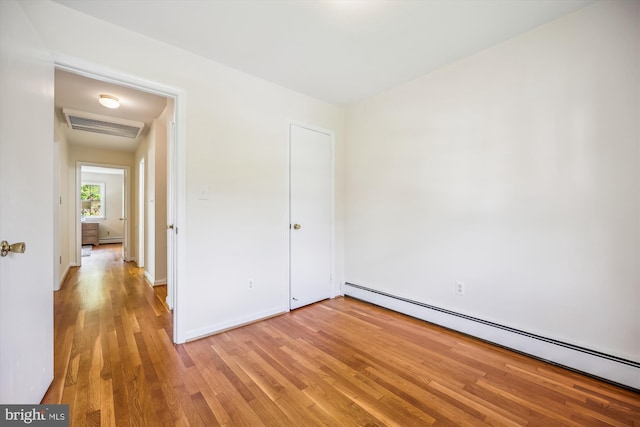 unfurnished bedroom with a baseboard heating unit, light wood finished floors, and baseboards