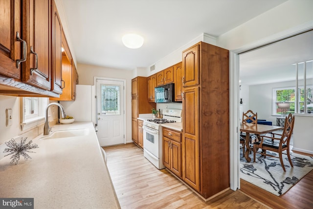 kitchen featuring white gas stove, a sink, black microwave, light countertops, and brown cabinetry