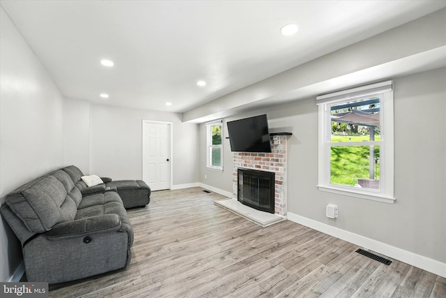 living area with plenty of natural light, a brick fireplace, wood finished floors, and visible vents
