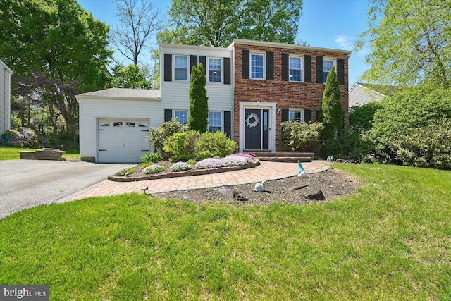 colonial inspired home with an attached garage, brick siding, aphalt driveway, and a front yard