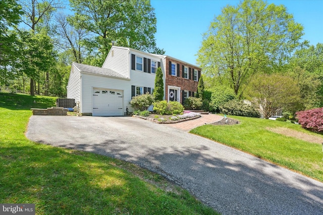 colonial-style house featuring central air condition unit, an attached garage, driveway, and a front lawn