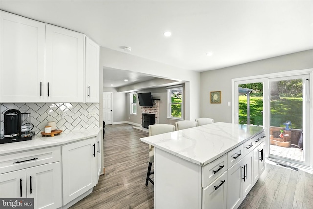 kitchen with a brick fireplace, white cabinetry, decorative backsplash, and a kitchen bar