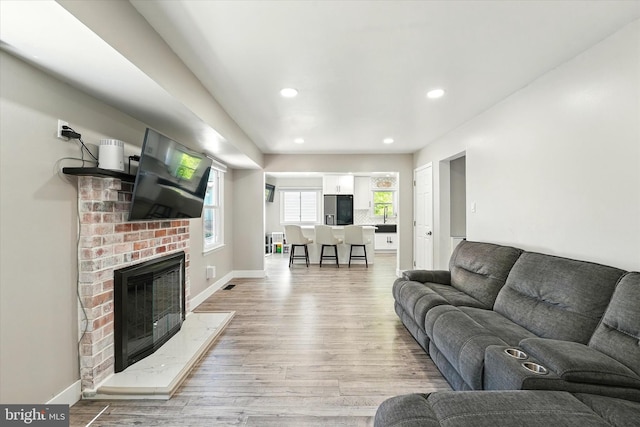 living room with a brick fireplace, recessed lighting, baseboards, light wood-type flooring, and visible vents