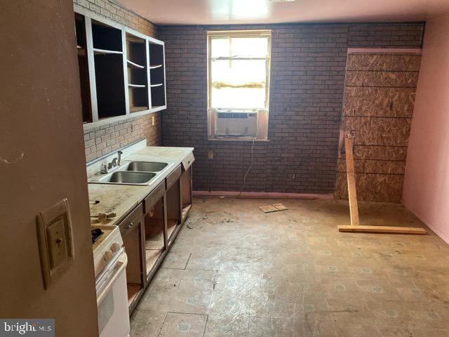 kitchen featuring brick wall, stove, a sink, and cooling unit