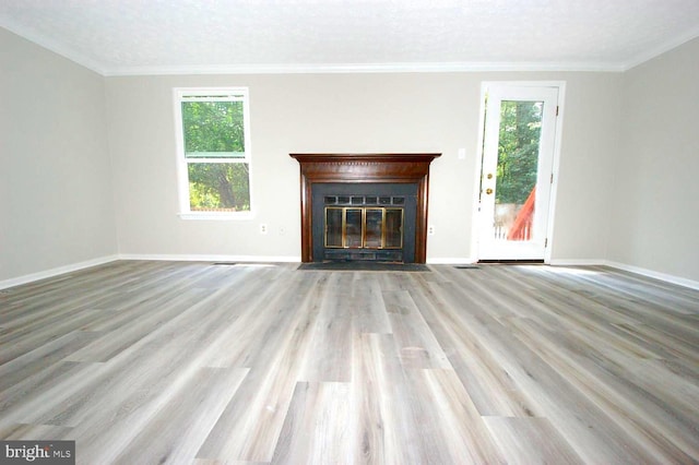 unfurnished living room with plenty of natural light, a fireplace with flush hearth, crown molding, and wood finished floors