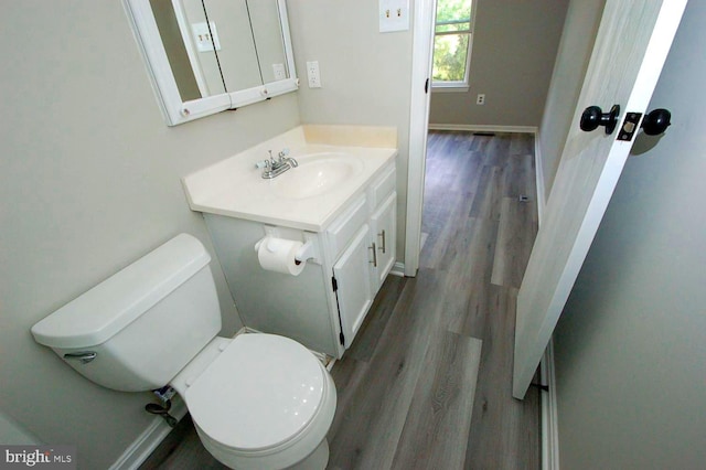 half bathroom with vanity, baseboards, wood finished floors, and toilet