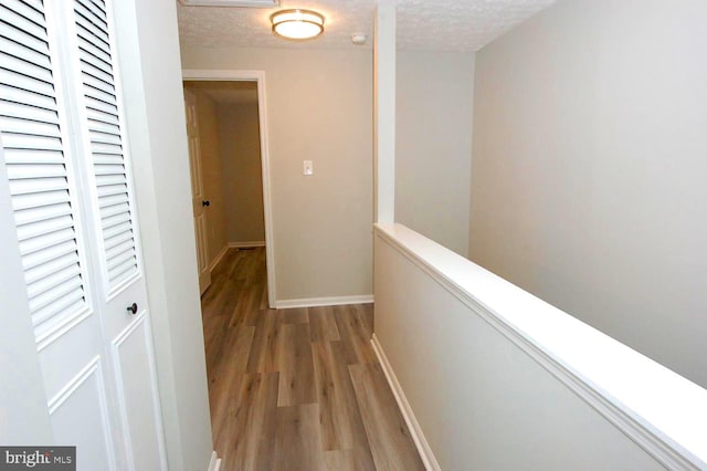 hallway with a textured ceiling, baseboards, light wood-style flooring, and an upstairs landing